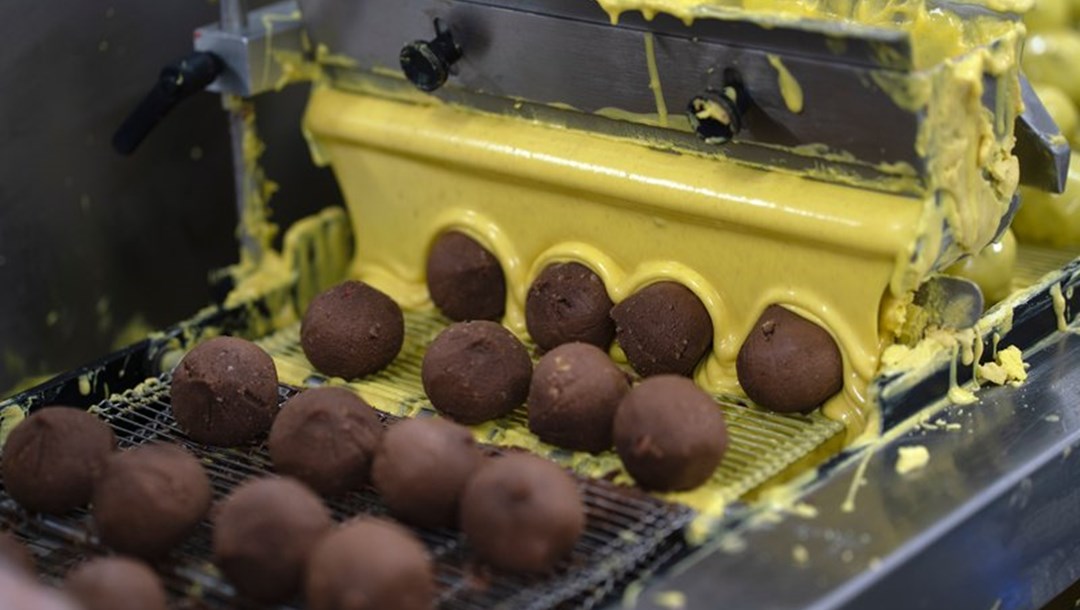 En anden maskine overtrækker dem med chokolade. Her er det gul chokolade, men bageriet har syv forskellige farver og smage, som de skifter imellem. I dag producerer bageriet lejlighedsromkugler, når danskerne for eksempel går til valg eller ser VM. 