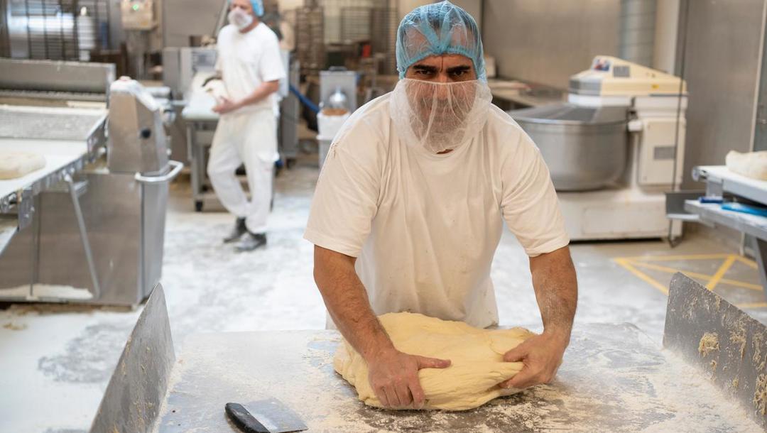 Mohammed Alasar lægger kræfterne i, når han ælter dejen til kanelsnurrer. Herefter klarer to maskiner at rulle dejen flad og sprøjte den med smørcreme med kanel.