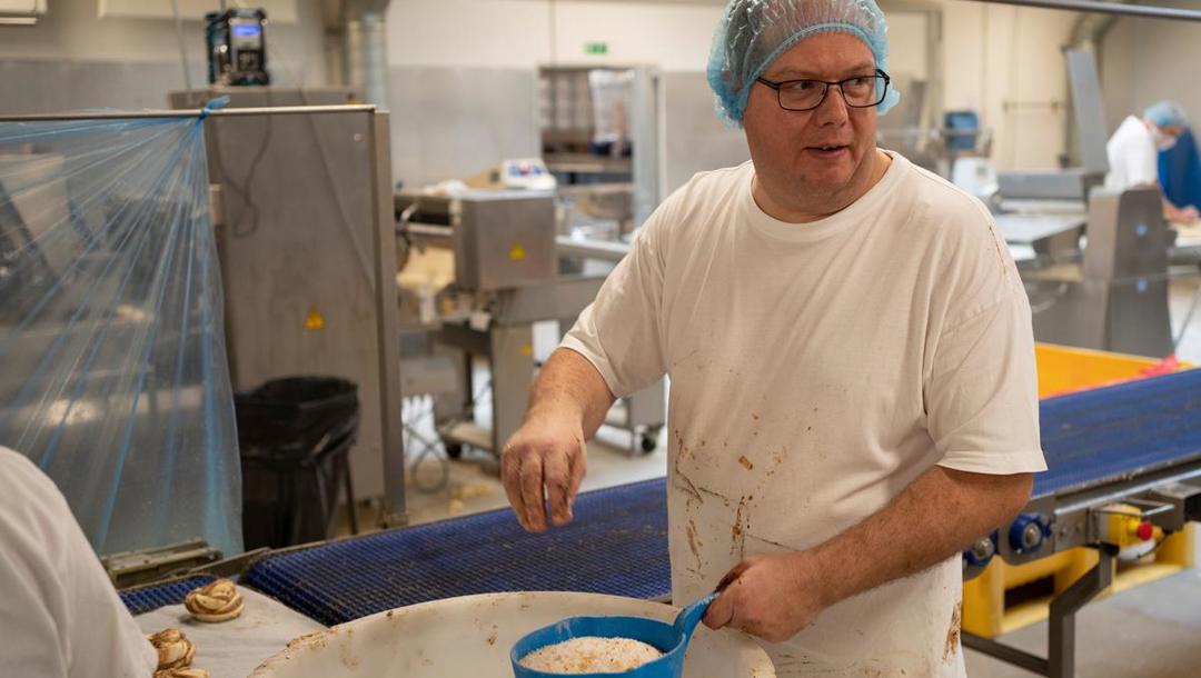 Efter en omgang æg, som sprøjtes på, er det tid til topping.  I dag er det Michael Nielsen, der står for at drysse overfladen med sukker og nødder. Snart har han en anden funktion. Det hold, der laver kanelsnurrer, roterer nemlig mellem stationerne.